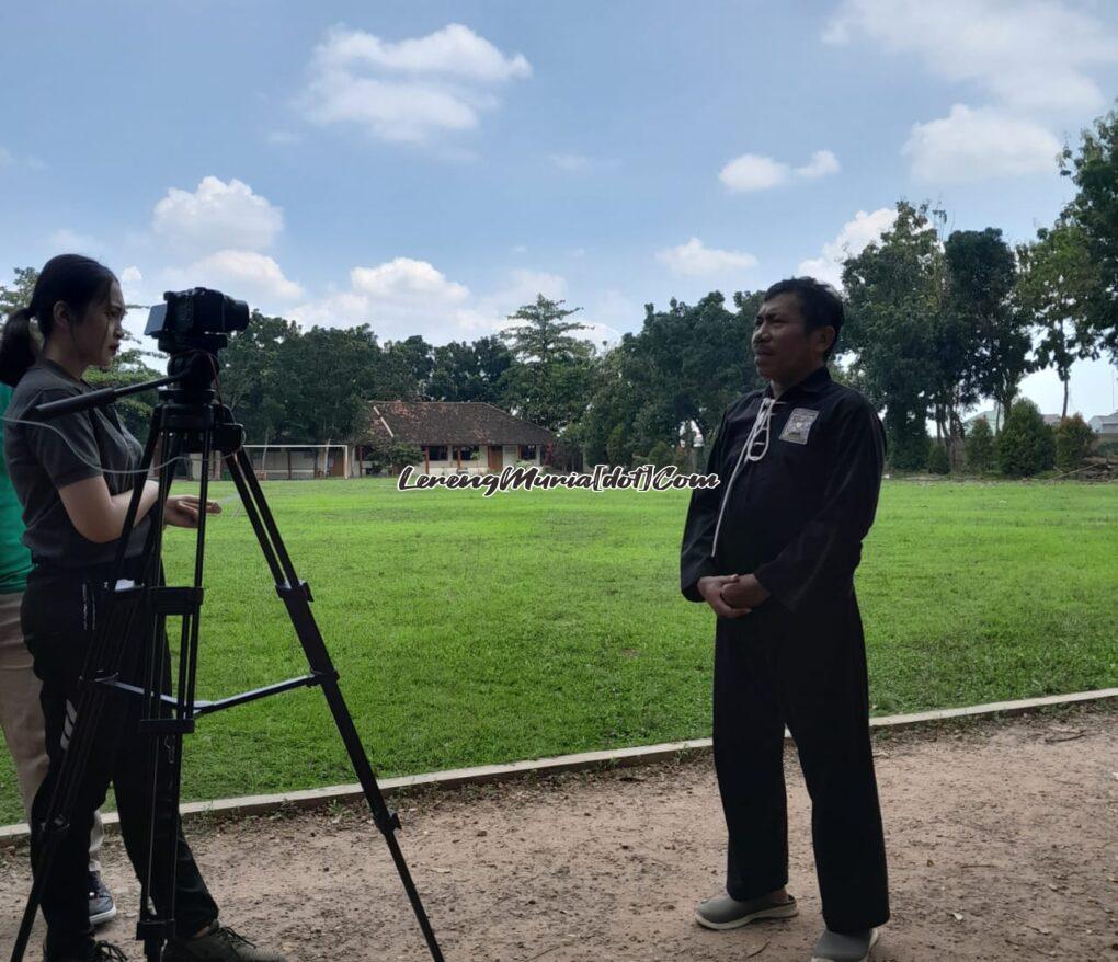 Foto Eko Wahono (kanan) diwawancarai di outdoor, pesilat background meninggalkan tempat